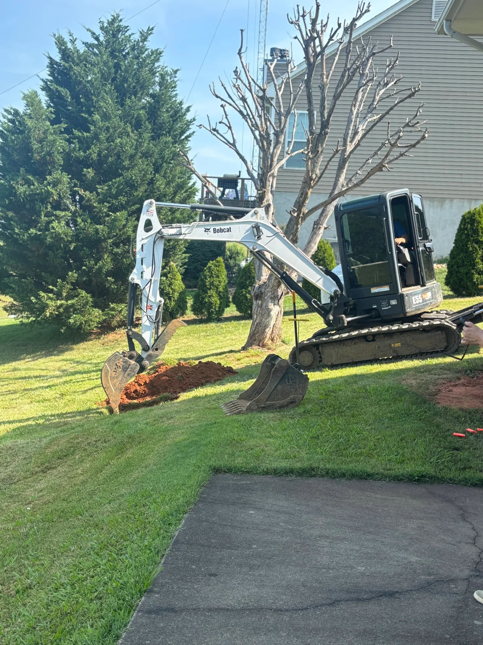 Bobcat E35 mini excavator digging a trench in a grassy yard beside a concrete driveway
